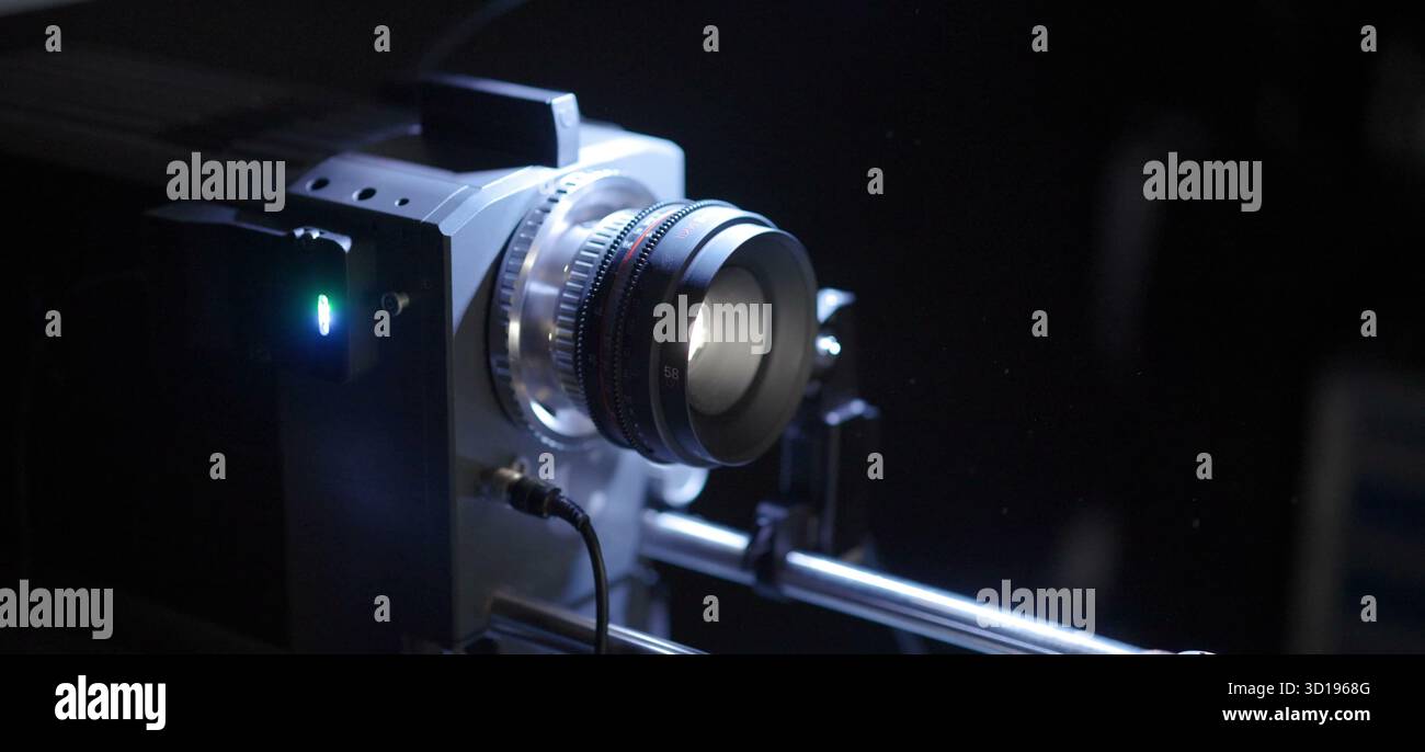 L'obiettivo professionale di una fotocamera cinematografica si illumina con precisione in un colore scuro. Foto Stock