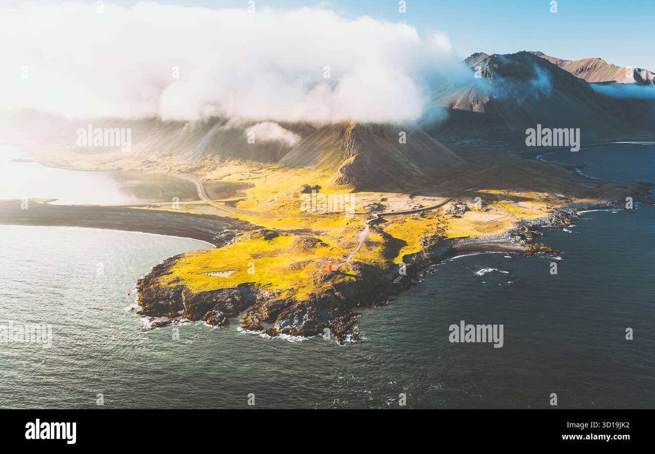 Veduta aerea del faro di Hvalnesviti che si erge con orgoglio contro le onde che si infrangono e il paesaggio aspro sotto il cielo, Hvalnesviti, Sveitarfélagið Hornafjörður, Islanda. Foto Stock