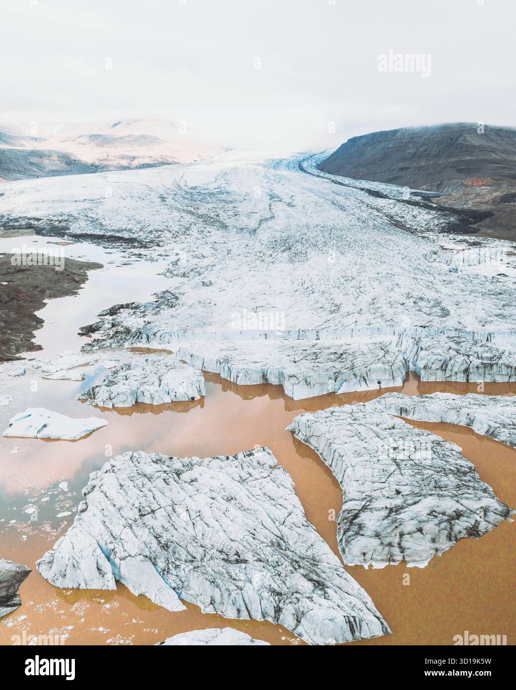 Vista aerea del ghiaccio glaciale che incontra le acque ocra, creando un netto contrasto con il paesaggio silenzioso, Heinabergsjökull, Sveitarfélagið Hornafjörður, Islanda. Foto Stock