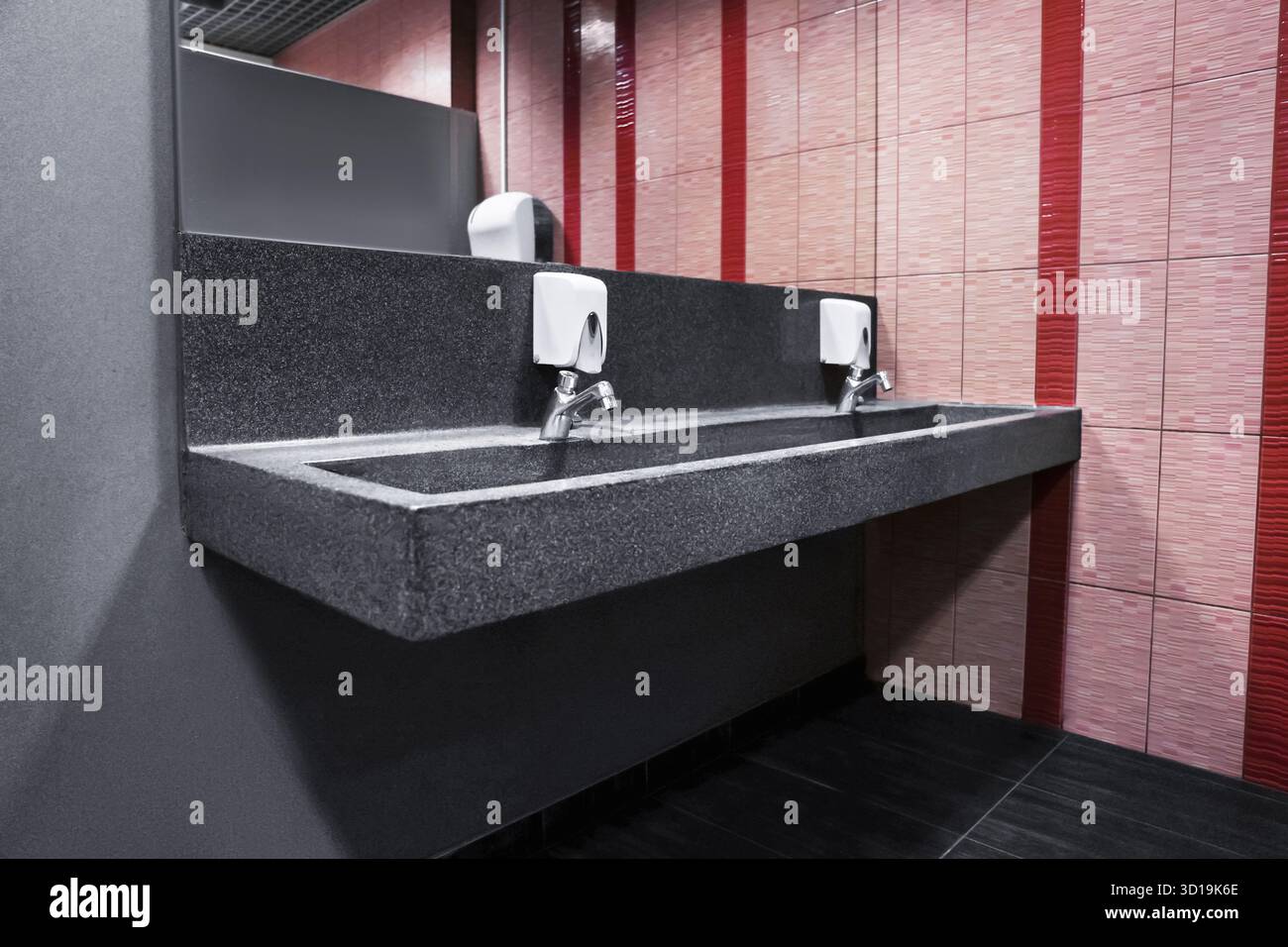 Moderno lavandino in granito per servizi igienici pubblici con acqua calda e fredda, su sfondo piastrellato. Foto di alta qualità Foto Stock