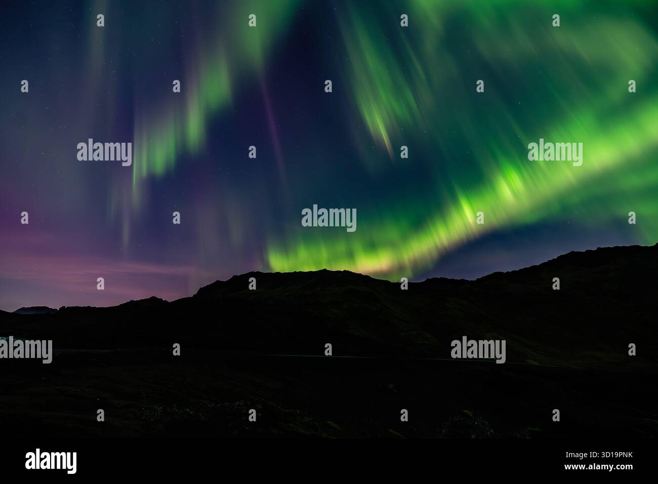 La vista aerea dell'aurora boreale verde e viola dipinge il cielo notturno sopra le montagne scure e sagomate, posizione omessa. Foto Stock