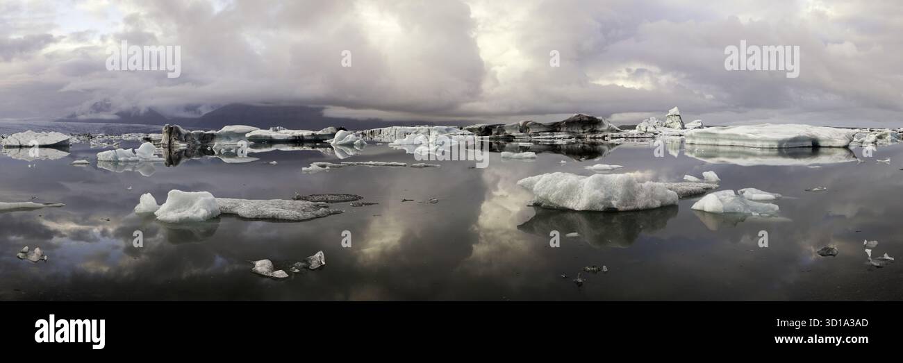 Vista degli iceberg luminosi che si staccano nelle acque serene e scure che riflettono il cielo minaccioso e nuvoloso di Jokulsarlon, Sveitarfélagið Hornafjörður, Islanda. Foto Stock