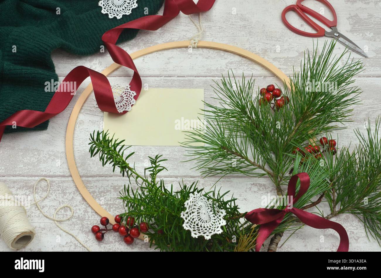 Giallo, foglio di carta vuoto da riempire con il contenuto. Corona di Natale, rami di conifere verdi, fiocco rosso, forbici e cordoncino sul tavolo di legno. Foto Stock