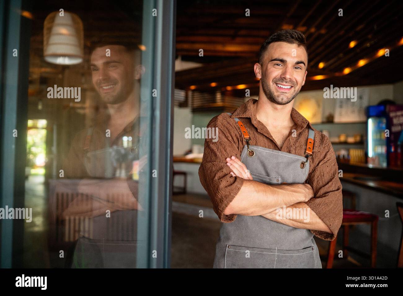 Orgoglioso proprietario di un caffè che si trova con fiducia dietro il bancone, pronto a servire i clienti con un sorriso caldo Foto Stock