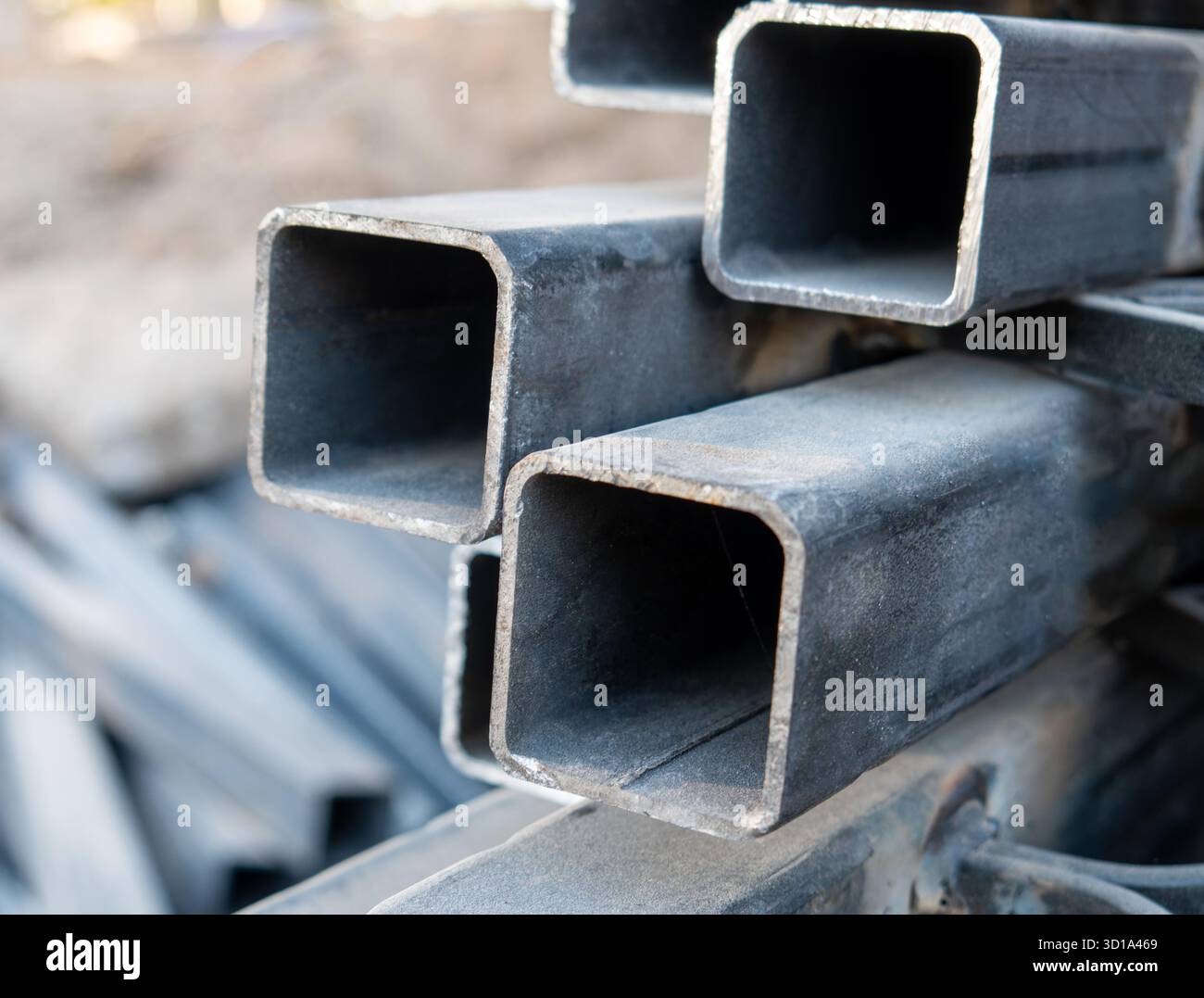 I profili in acciaio si sovrappongono l'uno sull'altro nel cantiere. Messa a fuoco selettiva su pila di profili in acciaio quadrati. Foto Stock