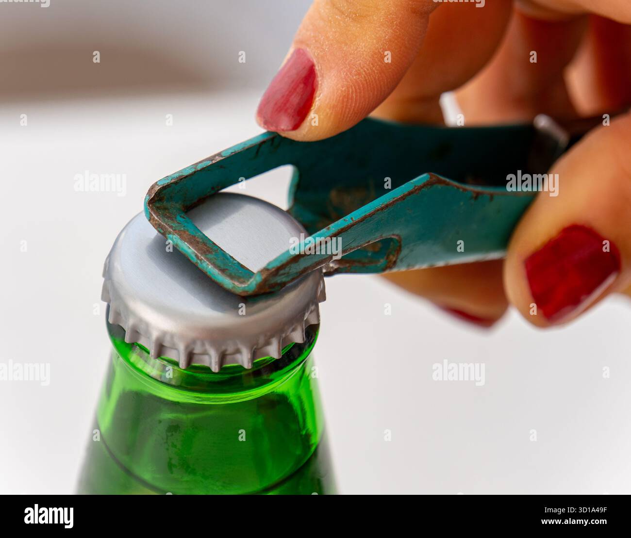 Una donna sta aprendo una bevanda fredda con un apribottiglie. Apribottiglie retrò in metallo di colore verde e bottiglia verde. Foto Stock