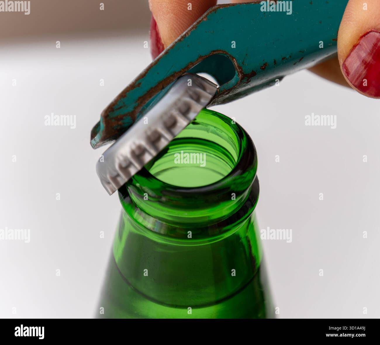 Una donna sta aprendo una bevanda fredda con un apribottiglie. Apribottiglie retrò in metallo di colore verde e bottiglia verde. Foto Stock