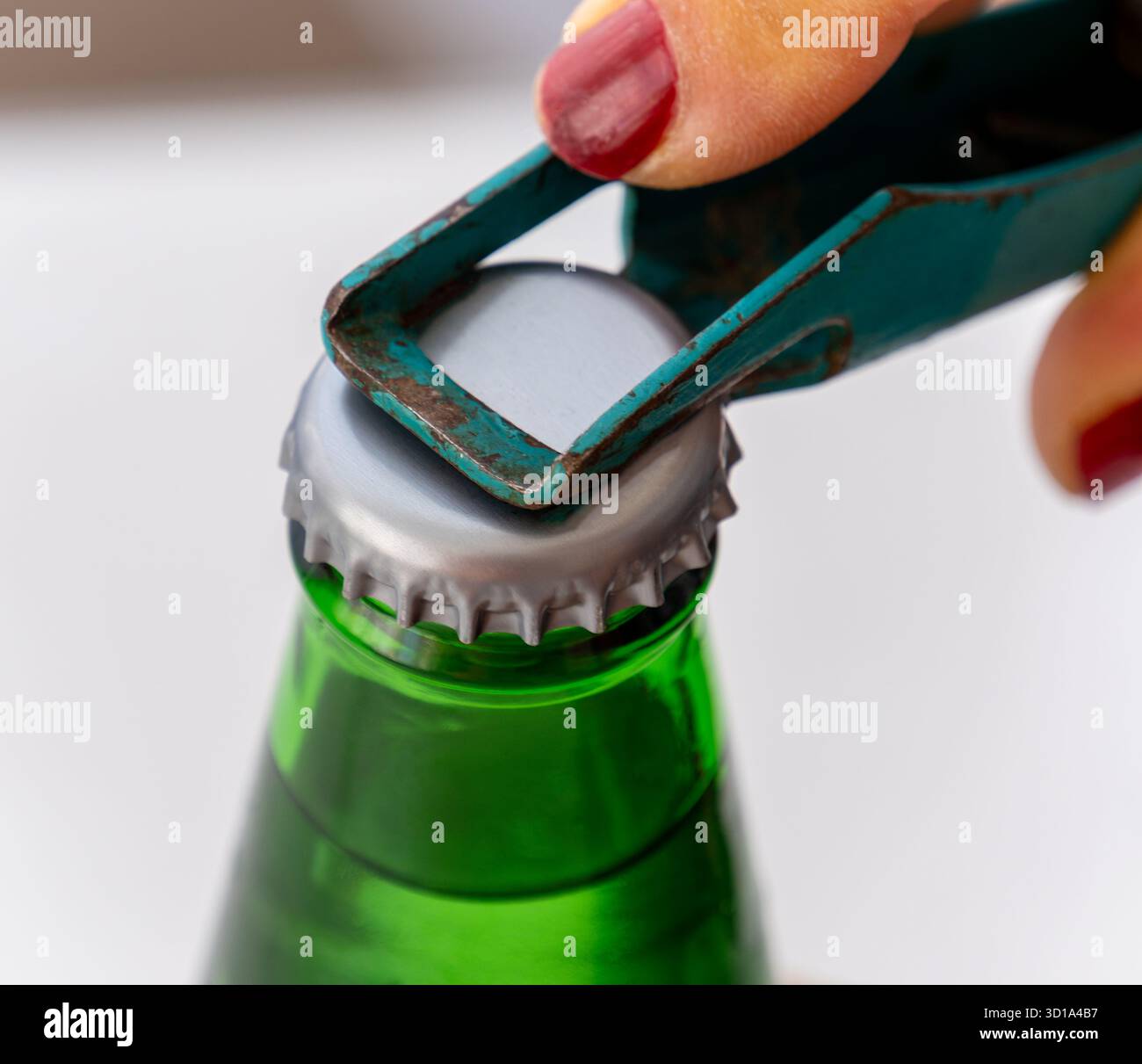 Una donna sta aprendo una bevanda fredda con un apribottiglie. Apribottiglie retrò in metallo di colore verde e bottiglia verde. Foto Stock