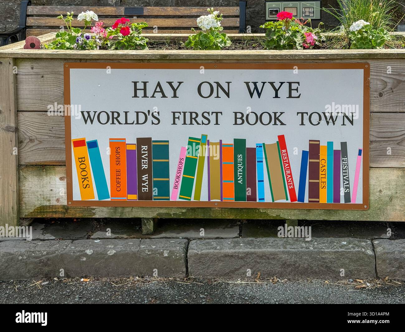 La vista di un vibrante cartello che proclamava "Hay-on-Wye, la prima città del libro del mondo" adorna una scatola di fioriere piena di fiori, invitando i visitatori a esplorare il paradiso letterario, Hay-on-Wye, Galles, Regno Unito. Foto Stock