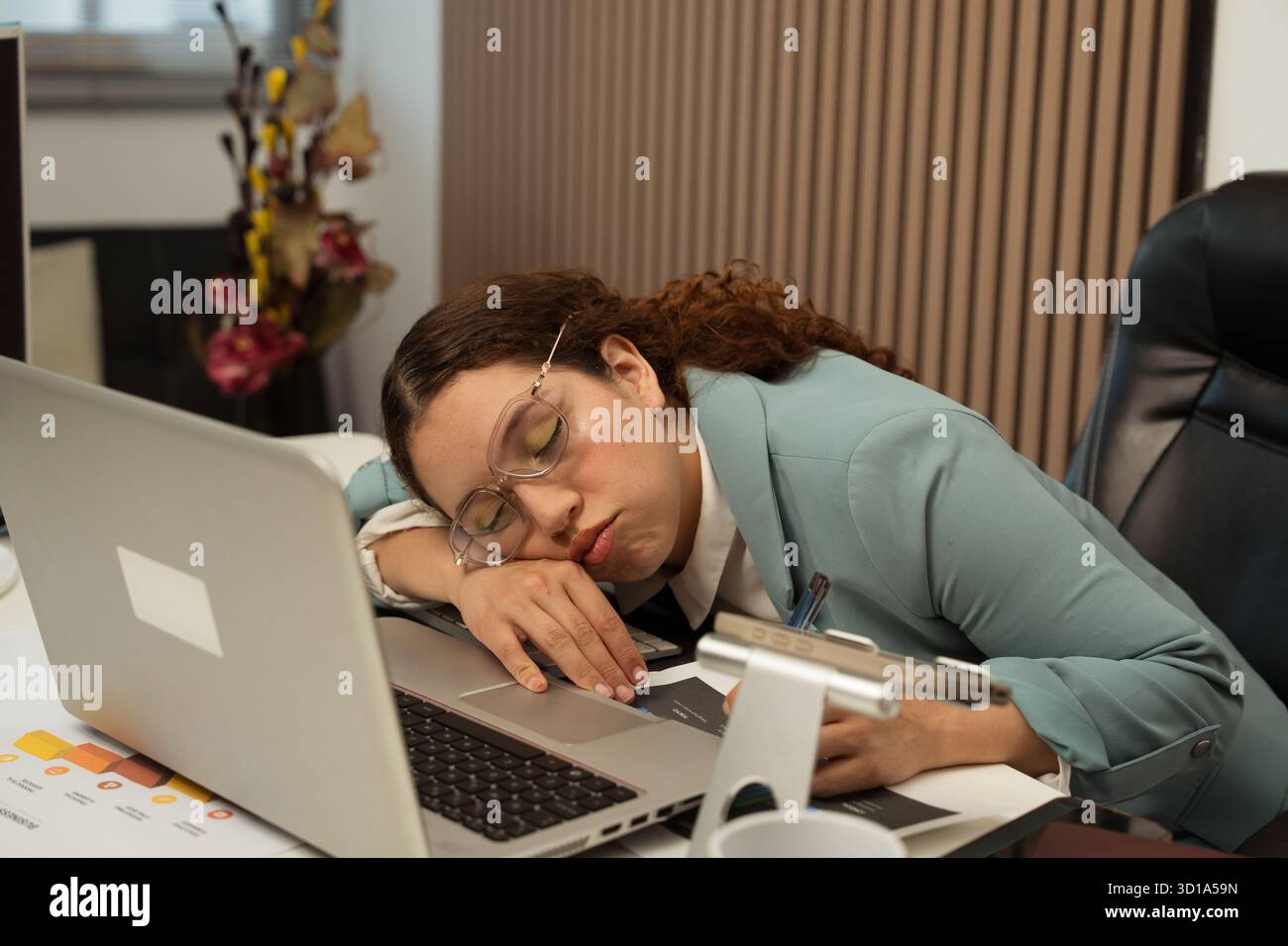 Giovane donna che dorme alla sua scrivania in ufficio, sperimentando bruciature e stanchezza dal lavoro Foto Stock