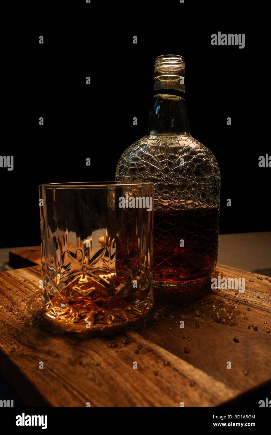 Bottiglia di whisky ambra e bicchiere su tavolo di legno - natura morta Moody drink Foto Stock