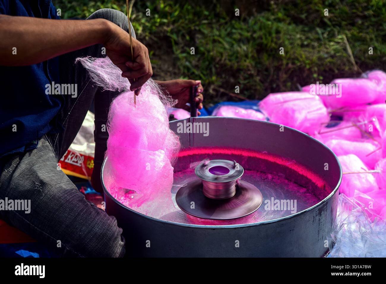 Persona che produce caramelle di cotone rosa su Spin Machine all'aperto al Market Stall durante la giornata di sole Foto Stock