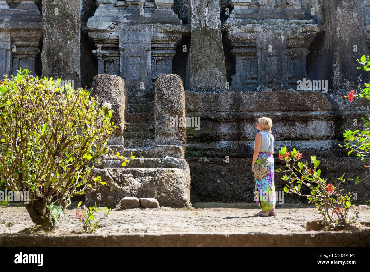 Una donna in pensione visita le antiche tombe scavate nella roccia di Gunung Kawi vicino a Ubud nell'isola di Bali, Indonesia. Vestita di sarong, osserva i sacri santuari Foto Stock