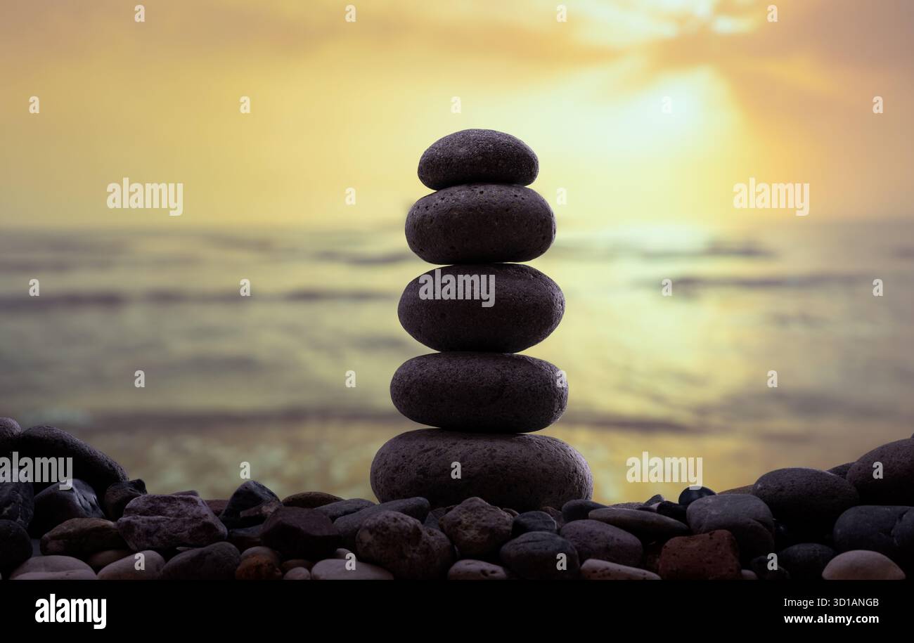Una pila di pietre lisce bilanciate sulla spiaggia al tramonto, simboleggiano l'armonia, l'equilibrio e la consapevolezza. Foto Stock