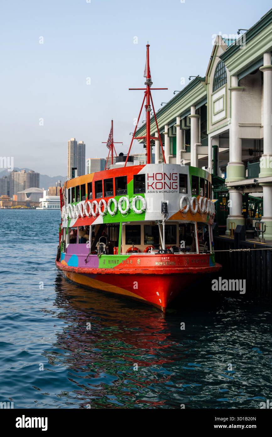La vista di un traghetto dai colori vivaci, adornato da sfumature luminose, poggia su un molo sotto un cielo limpido, in contrasto con l'acqua fresca, Hong Kong, ho Foto Stock