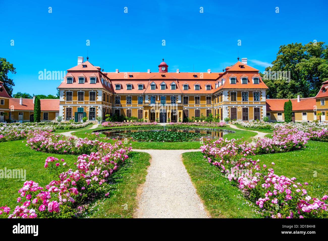 Vista panoramica del castello di Rajec Jestrebi in una soleggiata giornata estiva con cielo blu, rose rosa fiorenti e una fontana di fronte all'edificio storico. Foto Stock