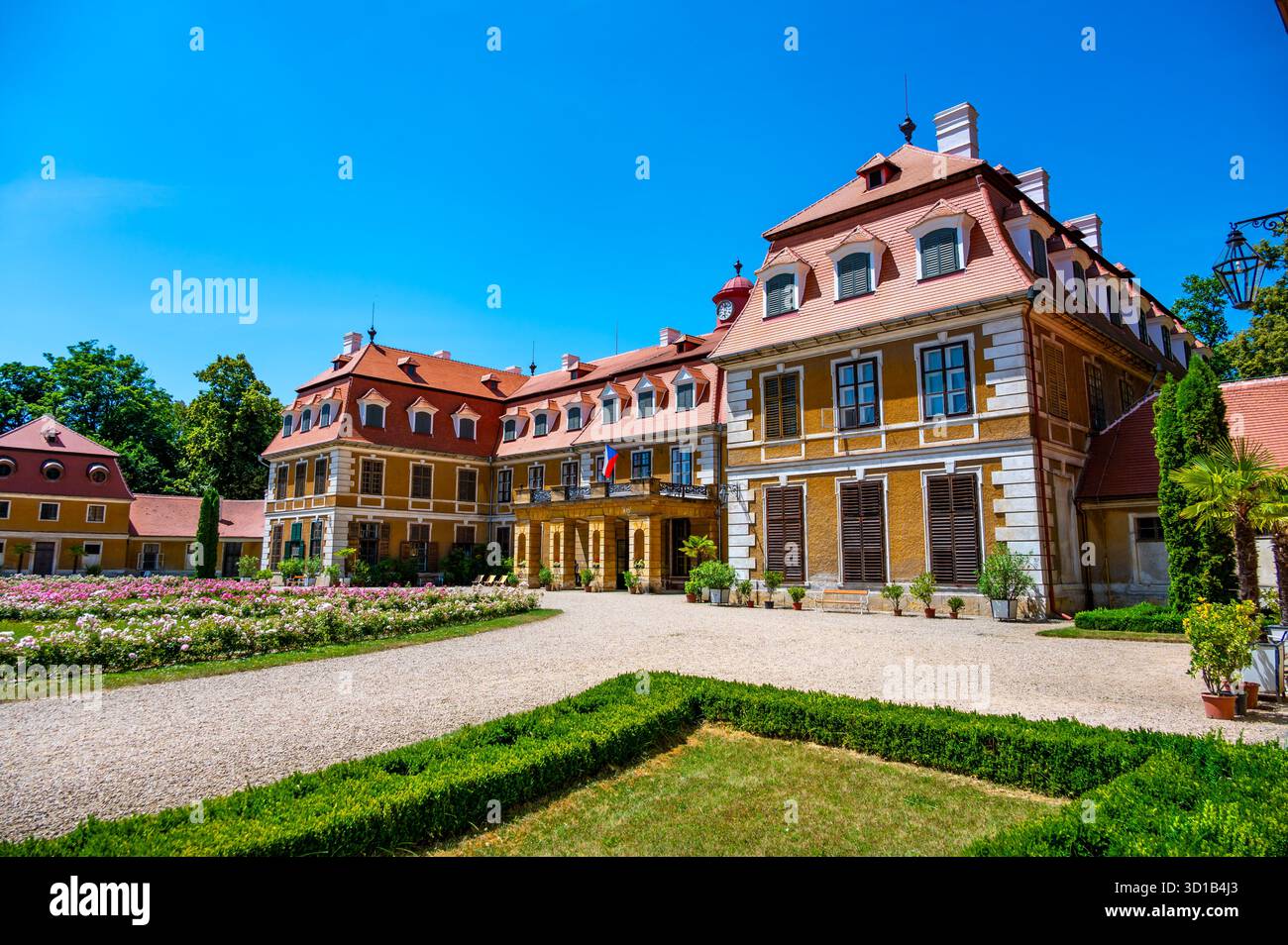 Vista panoramica del castello di Rajec Jestrebi in una soleggiata giornata estiva con cielo blu, rose rosa fiorenti e una fontana di fronte all'edificio storico. Foto Stock