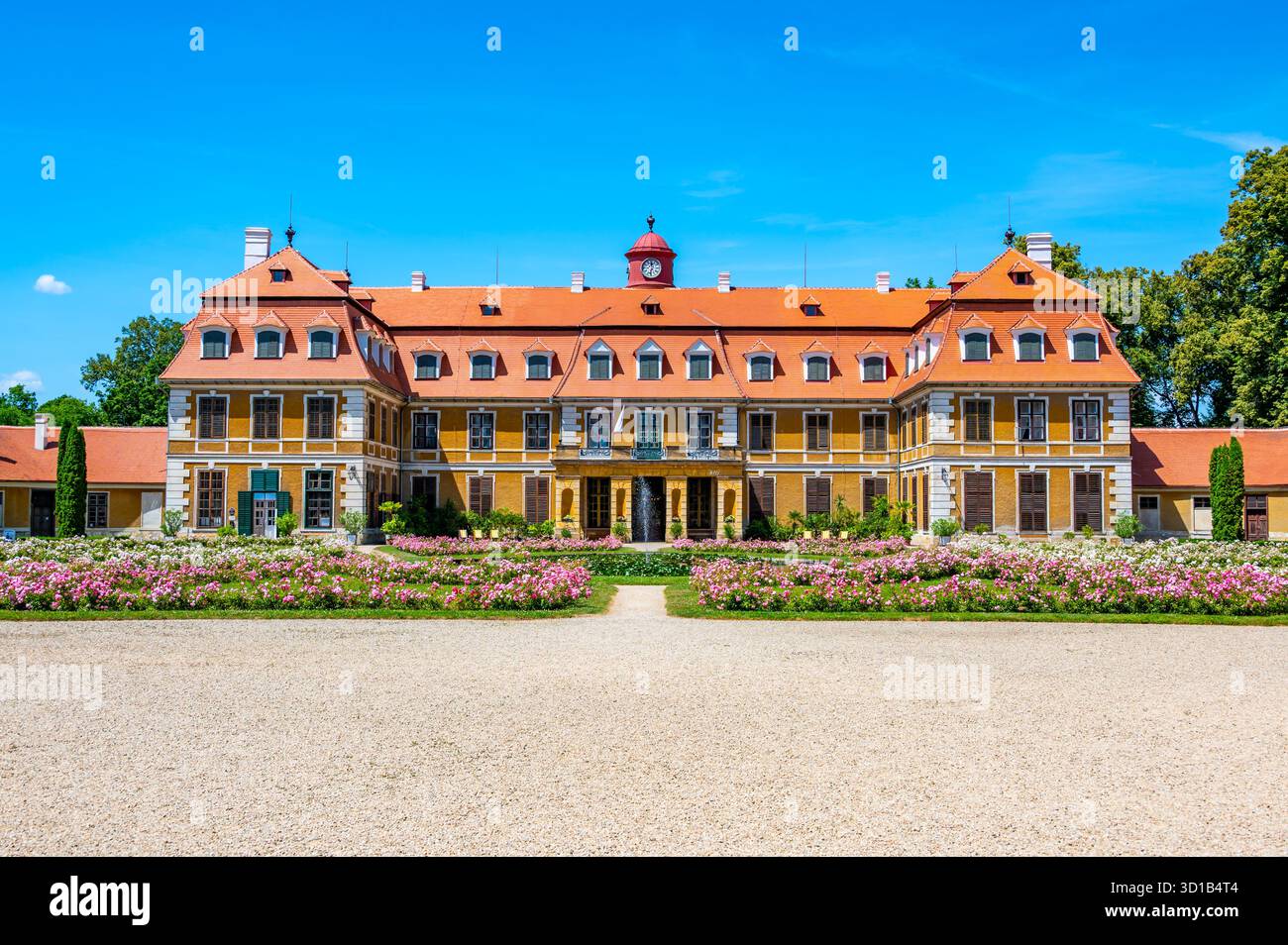 Vista panoramica del castello di Rajec Jestrebi in una soleggiata giornata estiva con cielo blu, rose rosa fiorenti e una fontana di fronte all'edificio storico. Foto Stock