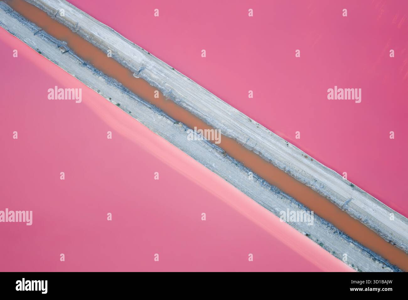 Veduta aerea di un piatto di sale rosa vivace tagliato da uno stretto canale e bordato da una striscia chiara, che crea un contrasto sorprendente di colore e consistenza, Aigues, Occitanie, Francia. Foto Stock