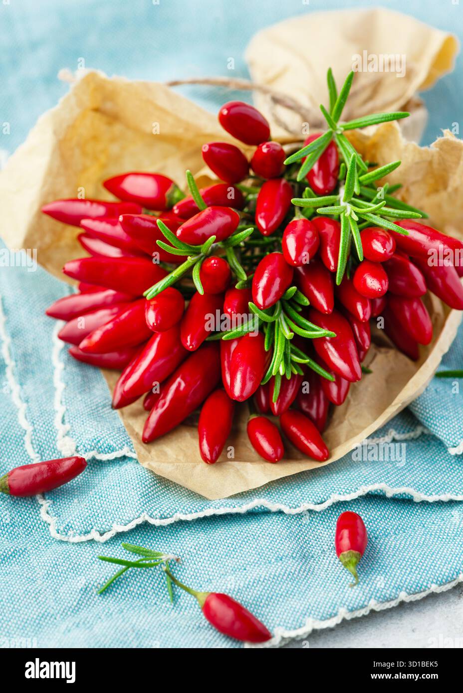 Pacchetto di peperoncini rossi con ciuffi di rosmarino su tessuto blu. Concetto di spezie naturali, alimentazione sana e fotografia di alimenti biologici Foto Stock