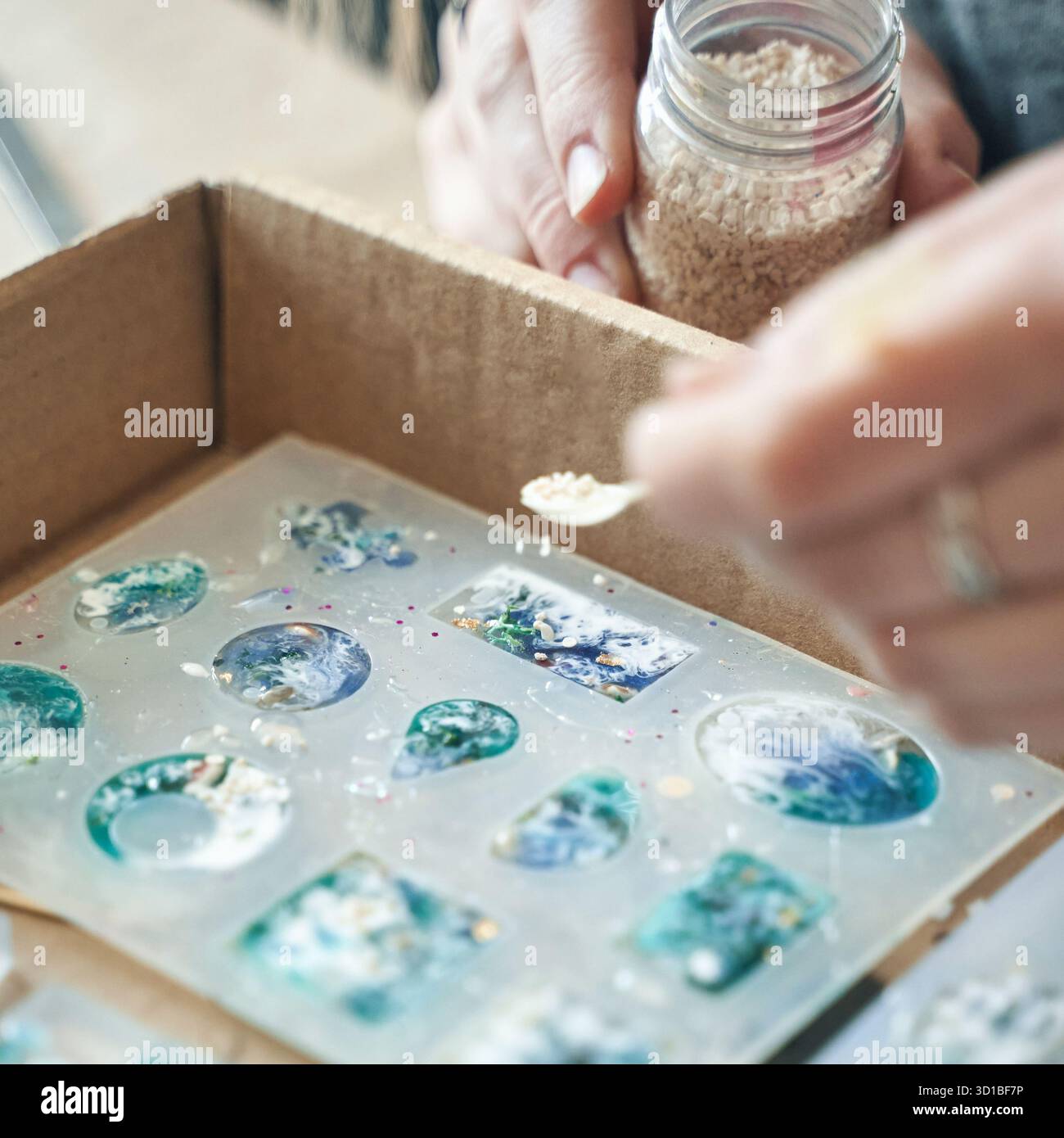 Le mani realizzano gioielli in resina colorata utilizzando stampi e decorazioni. Foto Stock