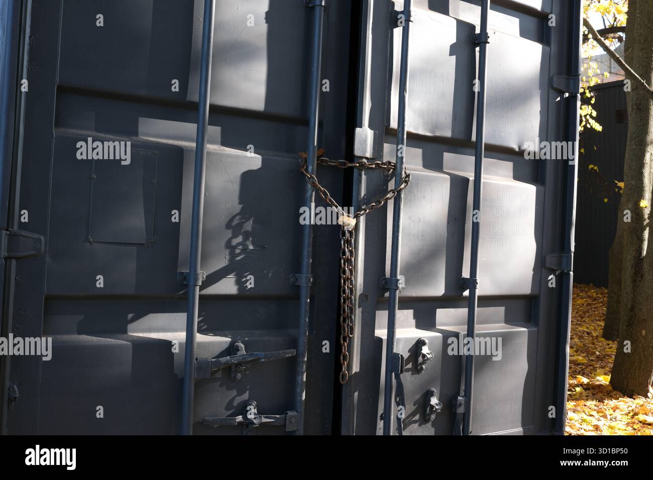 Due porte pesanti sono chiuse a chiave con una catena, circondate da un vivace fogliame autunnale. Foto Stock