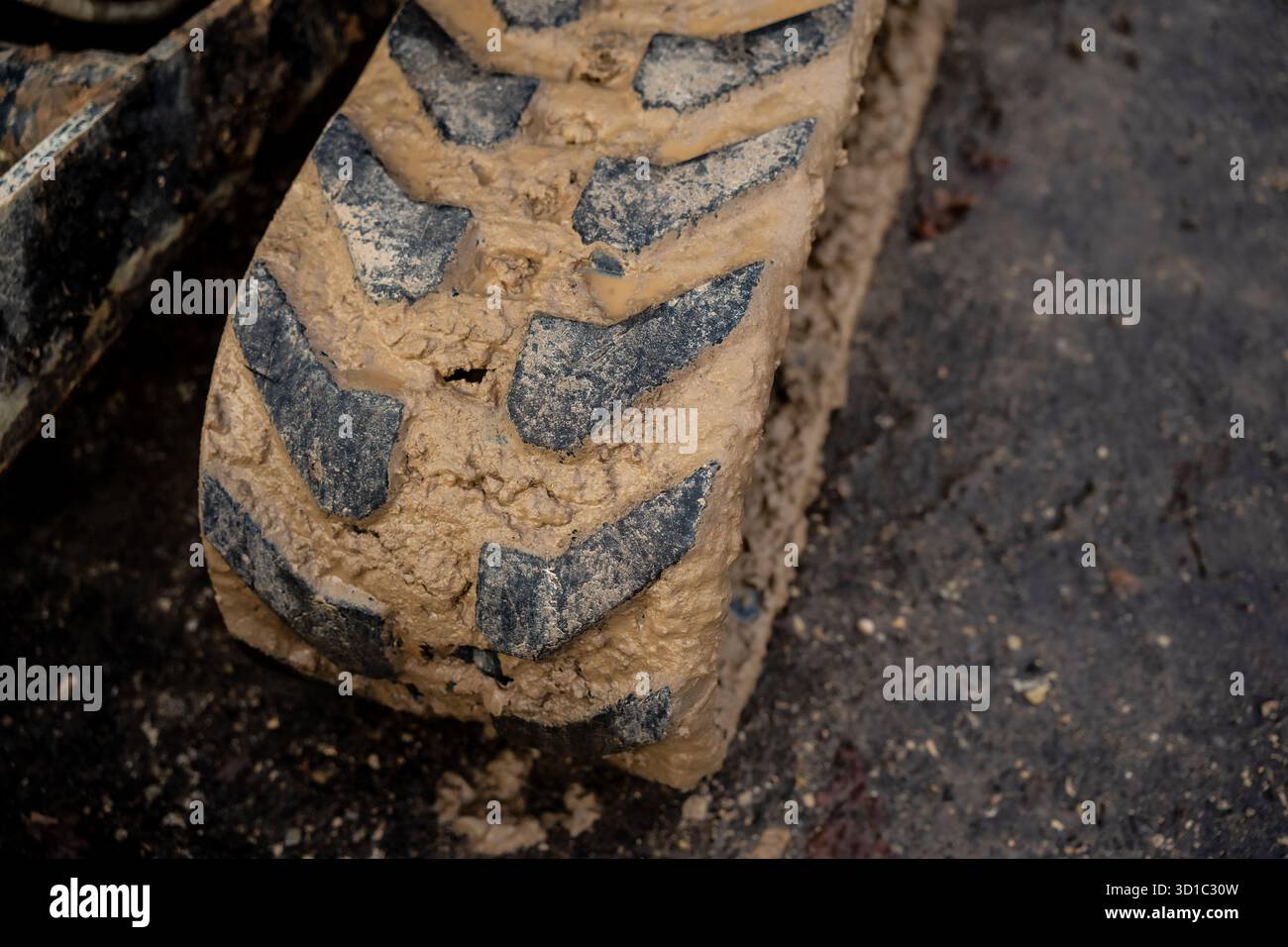 Pneumatico fangoso per escavatore su terreni edili che mostra sporcizia e terreno su un battistrada in gomma spessa che simboleggia il duro lavoro, l'uso di macchinari pesanti e l'uso industriale Foto Stock