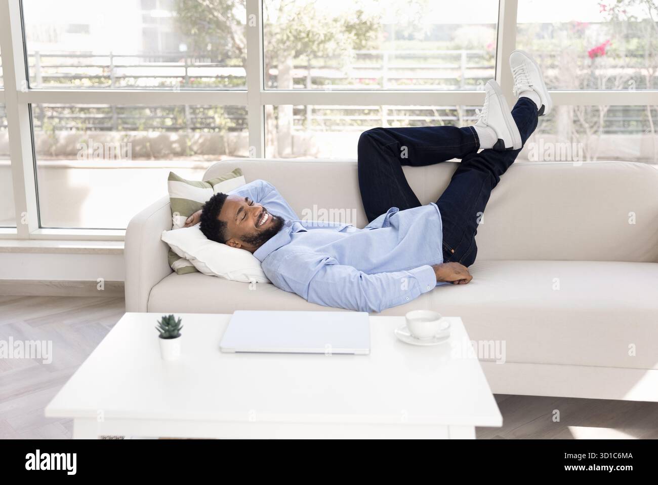 Uomo africano sorridente che si rilassa sdraiato su un comodo divano Foto Stock