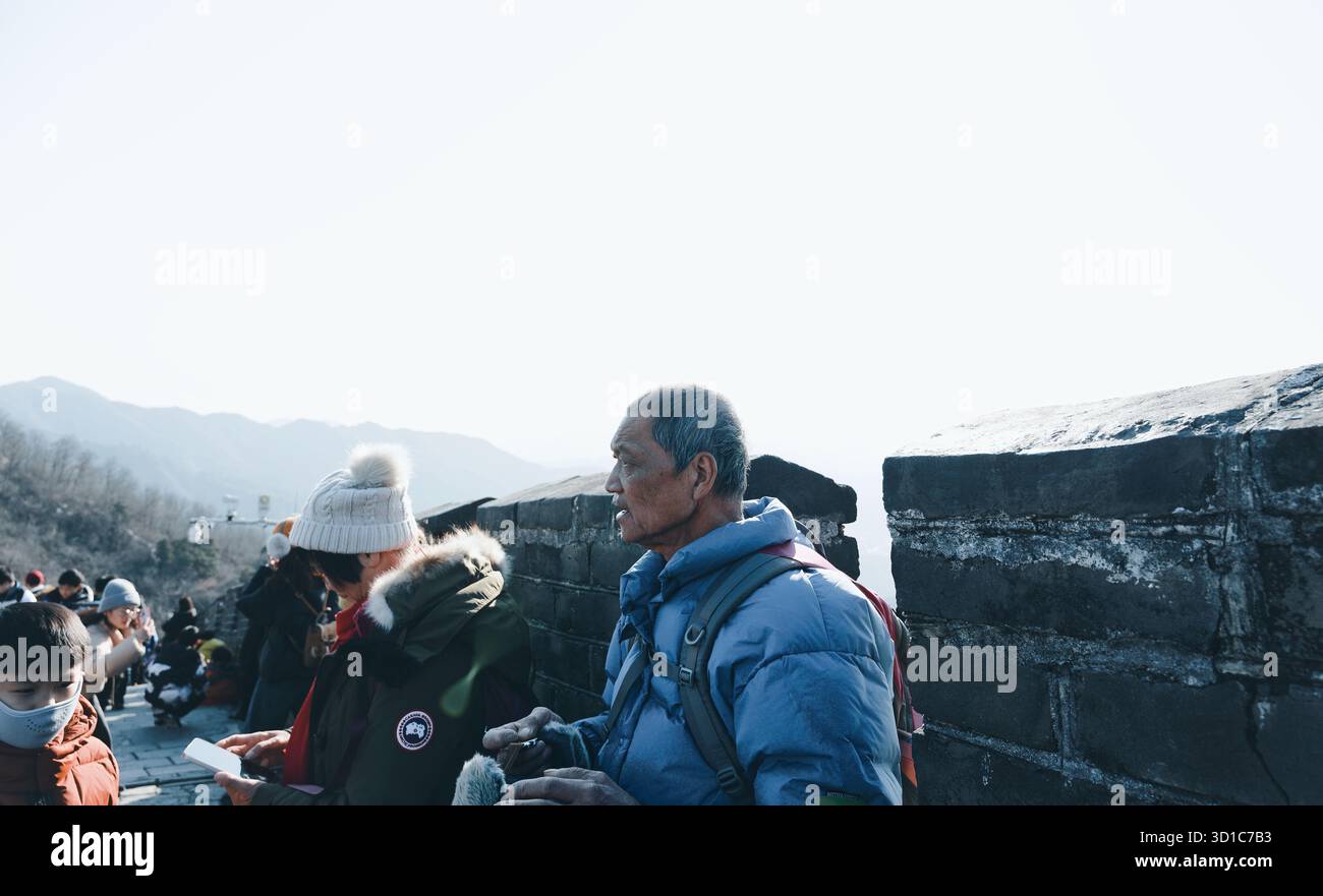Uomo anziano che guarda in lontananza, mentre i visitatori si fermano lungo la grande Muraglia Cinese Foto Stock
