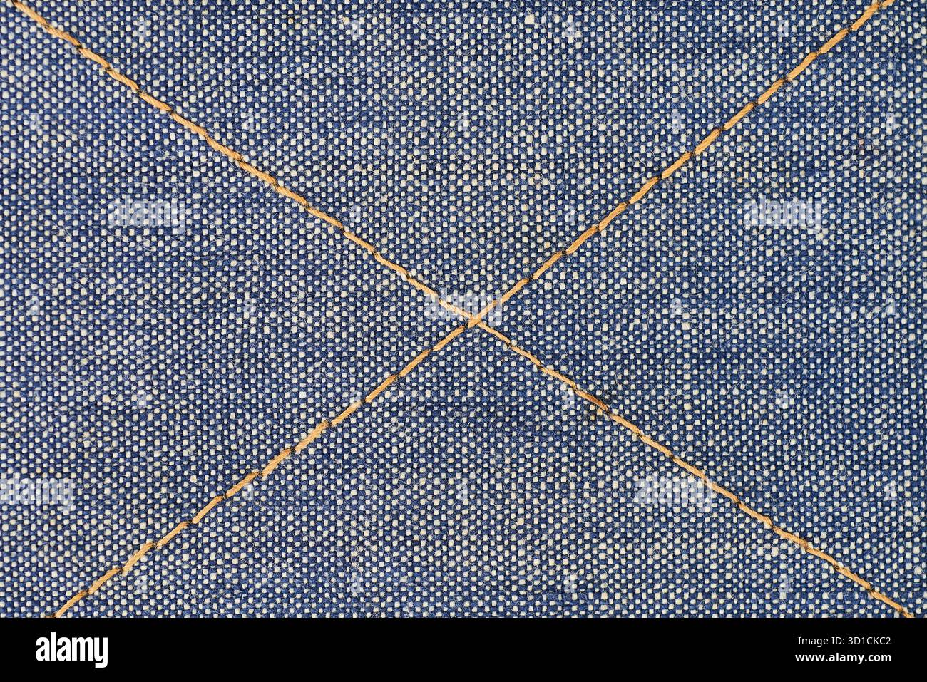 Il tessuto denim cucito mette in risalto il motivo a croce su un morbido materiale blu. Il filo a contrasto crea interesse visivo e mette in mostra gli artigiani Foto Stock