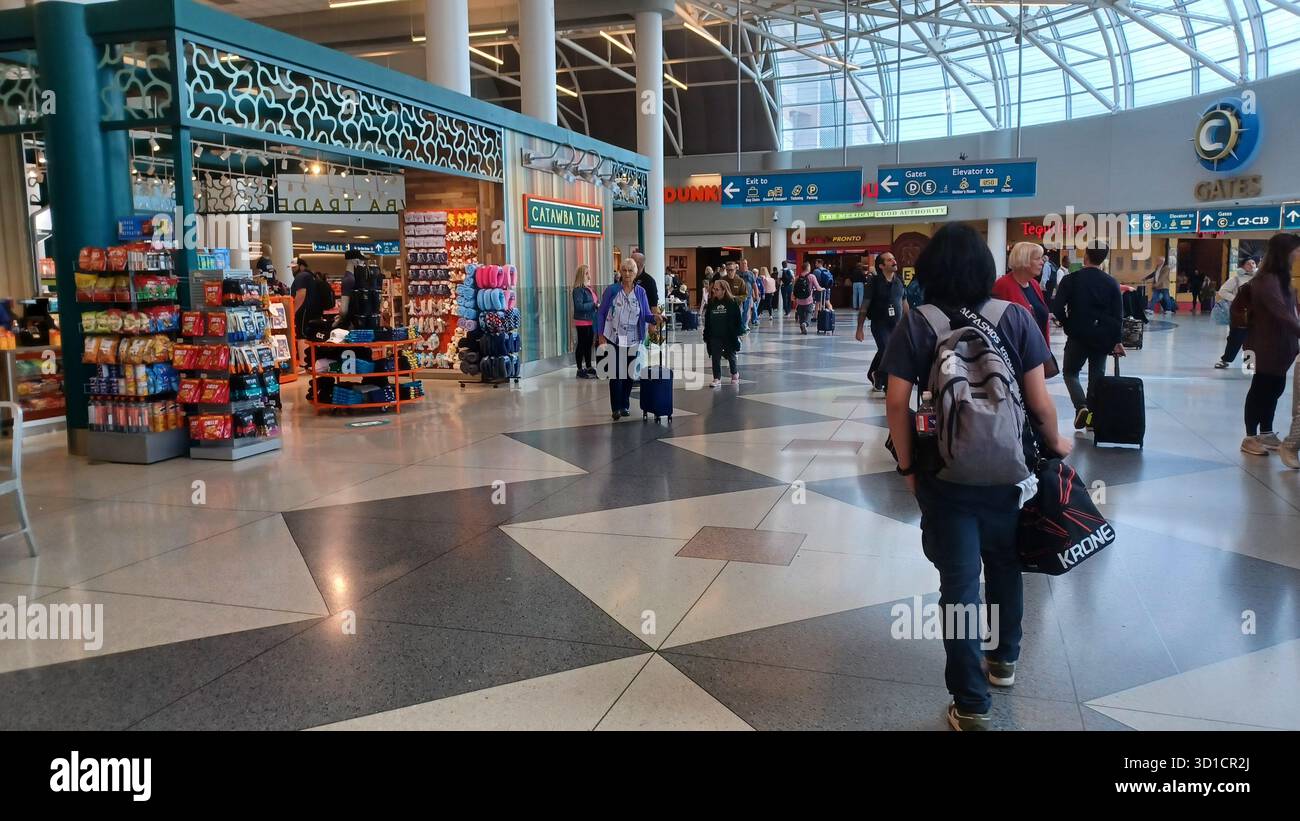 Charlotte, North Carolina, USA, 10 ottobre 2025: Le persone con bagagli attraversano un atrio luminoso e spazioso all'Aeroporto Internazionale Douglas di Charlotte. Foto Stock