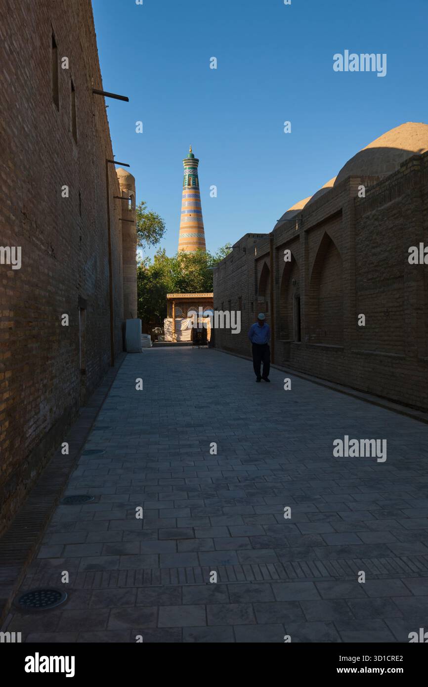 Una vista mattutina del minareto Islam Khoja, un uomo in primo piano, nell'ombra. Nella città fortificata, Ichan Qala, di Khiva, Uzbekistan. Foto Stock