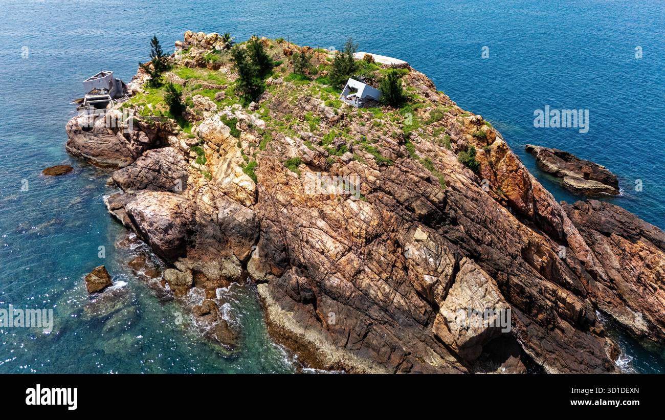 Isolotto roccioso vicino a Quy Nhon, Vietnam: Affioramento isolato con capanne per la pesca, mare turchese, natura aspra e avventura costiera, vista aerea Foto Stock