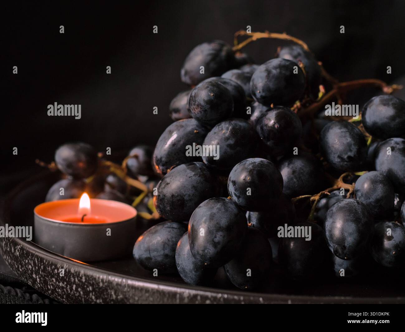 Uva scura con una candela accesa - romantica e accogliente scena autunnale con uva e lume di candela Foto Stock