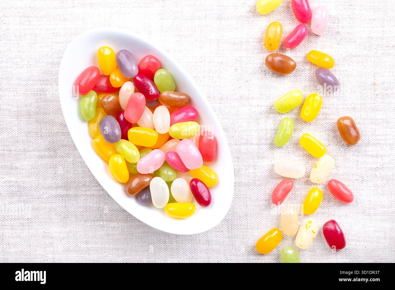 Gelatina, assortimento di sapori e colori, in ciotola bianca ovale, su lino. Caramelle a forma di fagiolo con conchiglie di caramelle morbide e interni in gel spessi Foto Stock