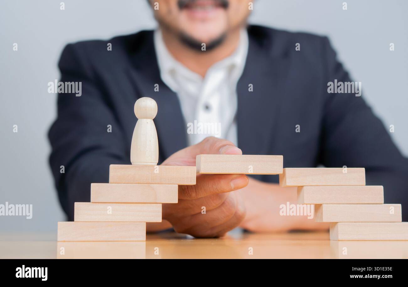 Uomo che risolve i problemi costruendo un ponte con blocchi di legno per coprire un vuoto per le piccole persone icona di legno che camminano attraverso. Foto Stock