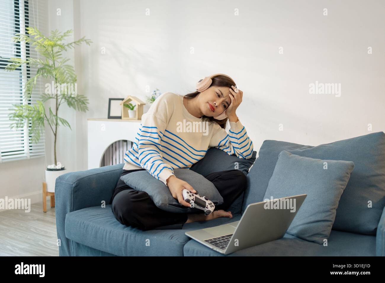 Una giovane donna che indossa le cuffie sta giocando a un videogame sul suo notebook, tenendo in mano un controller con espressioni emotive di gioia, eccitazione e fruste Foto Stock