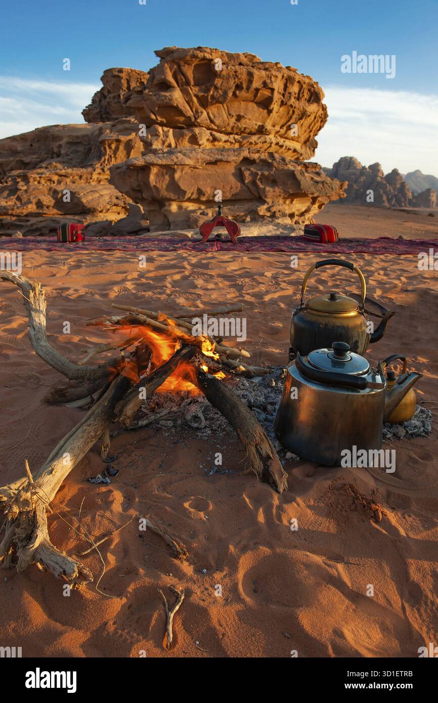 Due teiere accanto a un fuoco aperto nella sabbia del deserto, rocce erose sullo sfondo, Wadi Rum, Giordania Foto Stock