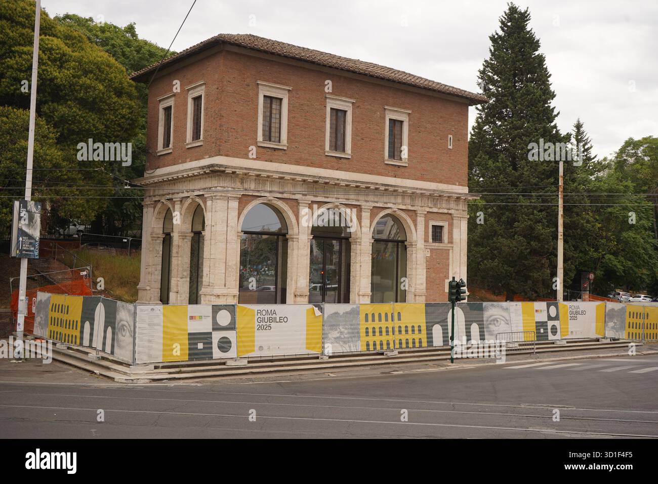 Piccolo edificio in mattoni, incorniciato da barriere di costruzione con cartello "ROMA GIUBILEO 2025", che suggerisce la preparazione per l'evento giubilare. Foto Stock