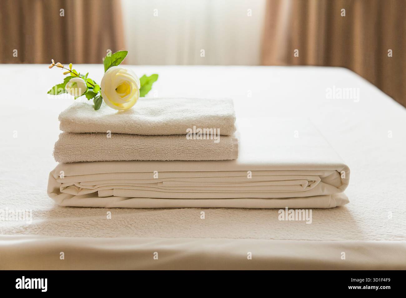 Asciugamani e biancheria bianchi freschi sono disposti ordinatamente su un tavolo, accompagnati da un delicato fiore. La sala ben illuminata crea un'atmosfera calda e accogliente Foto Stock