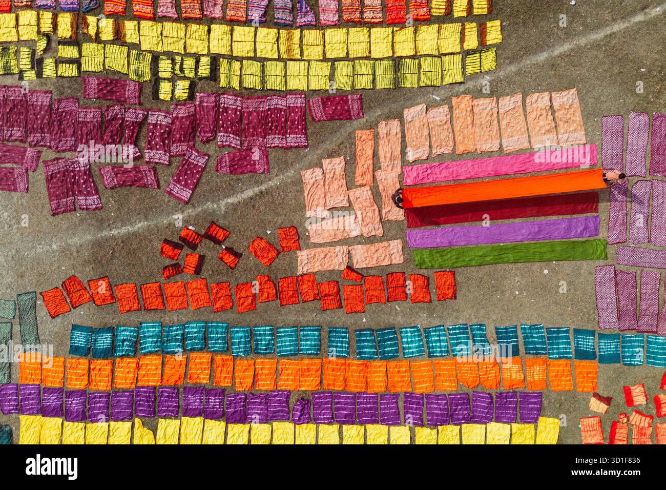 Narayanganj, Dacca, Bangladesh. 28 ottobre 2025. Centinaia di fogli di stoffa tinte a colori sono sparsi in un campo per l'asciugatura a Narayanganj, Bangladesh. I panni colorati che vendono per meno di 3 dollari sono disposti su macchie di erba per asciugarsi completamente, poiché è più economico e più sostenibile asciugarli alla luce del sole. Una volta asciugati, i tessuti vengono trasformati in capi come t-shirt e abiti prima di essere venduti in tutto il mondo. (Credit Image: © Joy Saha/ZUMA Press Wire) SOLO PER USO EDITORIALE! Non per USO commerciale! Foto Stock