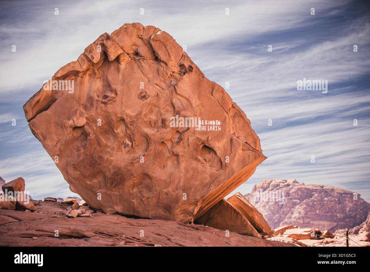 Grande roccia di arenaria con messaggio dipinto "Be Kind to the Earth" in Wadi Rum, Giordania, 2024. Segnale di sensibilizzazione ambientale nel paesaggio desertico. Foto Stock
