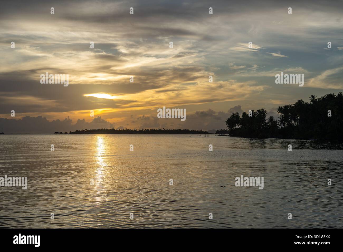 Uno splendido tramonto sull'isola di Tahaa nella Polinesia francese, con acque calme e barche a vela che creano un'atmosfera serena Foto Stock