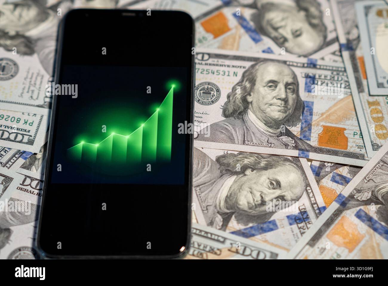 Uno smartphone mostra un grafico in aumento che simboleggia la crescita finanziaria, posizionato sullo sfondo di banconote in dollari. Foto Stock