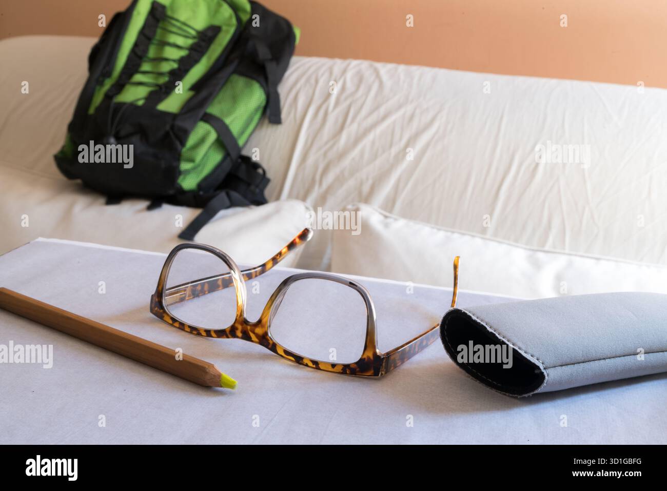Un paio di eleganti occhiali da vista con telaio a guscio di tartaruga poggia su un pezzo di carta bianca, accanto a una matita in legno con punta gialla e a un morbido vetro grigio Foto Stock
