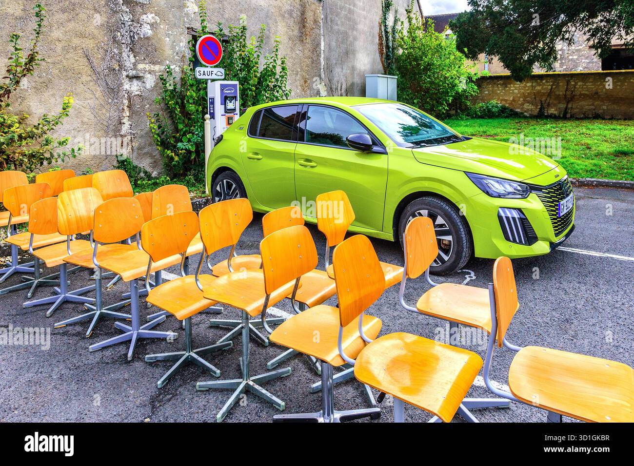Gruppo di 18 sedie da ufficio piegate in compensato in vendita presso un stivale brocante/auto sa... Accanto alla ricarica di una nuova Peugeot e-car in una presa di corrente - Francia centrale. Foto Stock