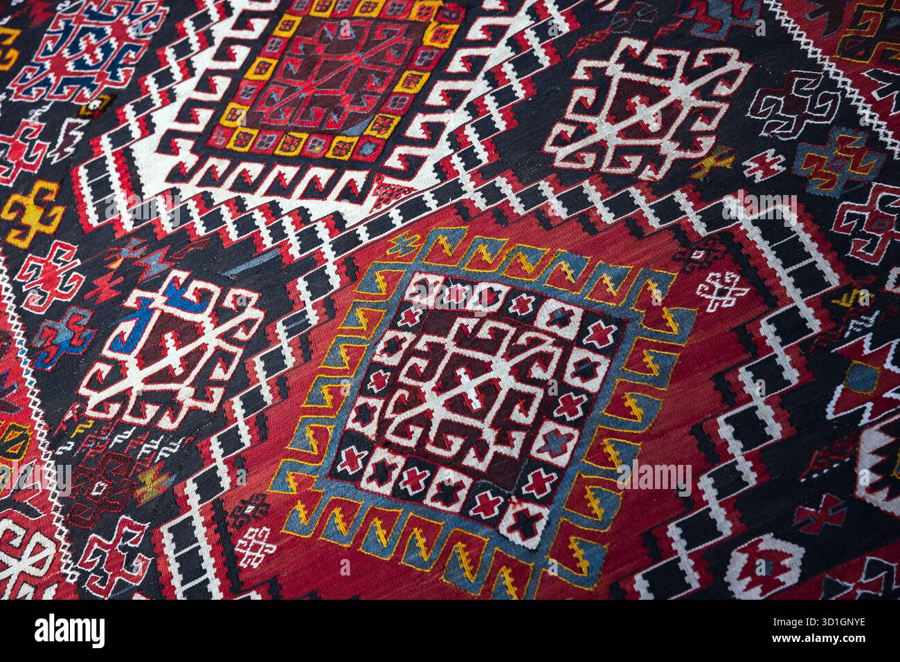 Un vivace tappeto kilim intrecciato a mano con motivi geometrici ripetuti, rossi, blu e gialli brillanti. Texture ricche e bordi audaci creano un'atmosfera calda e di culto Foto Stock