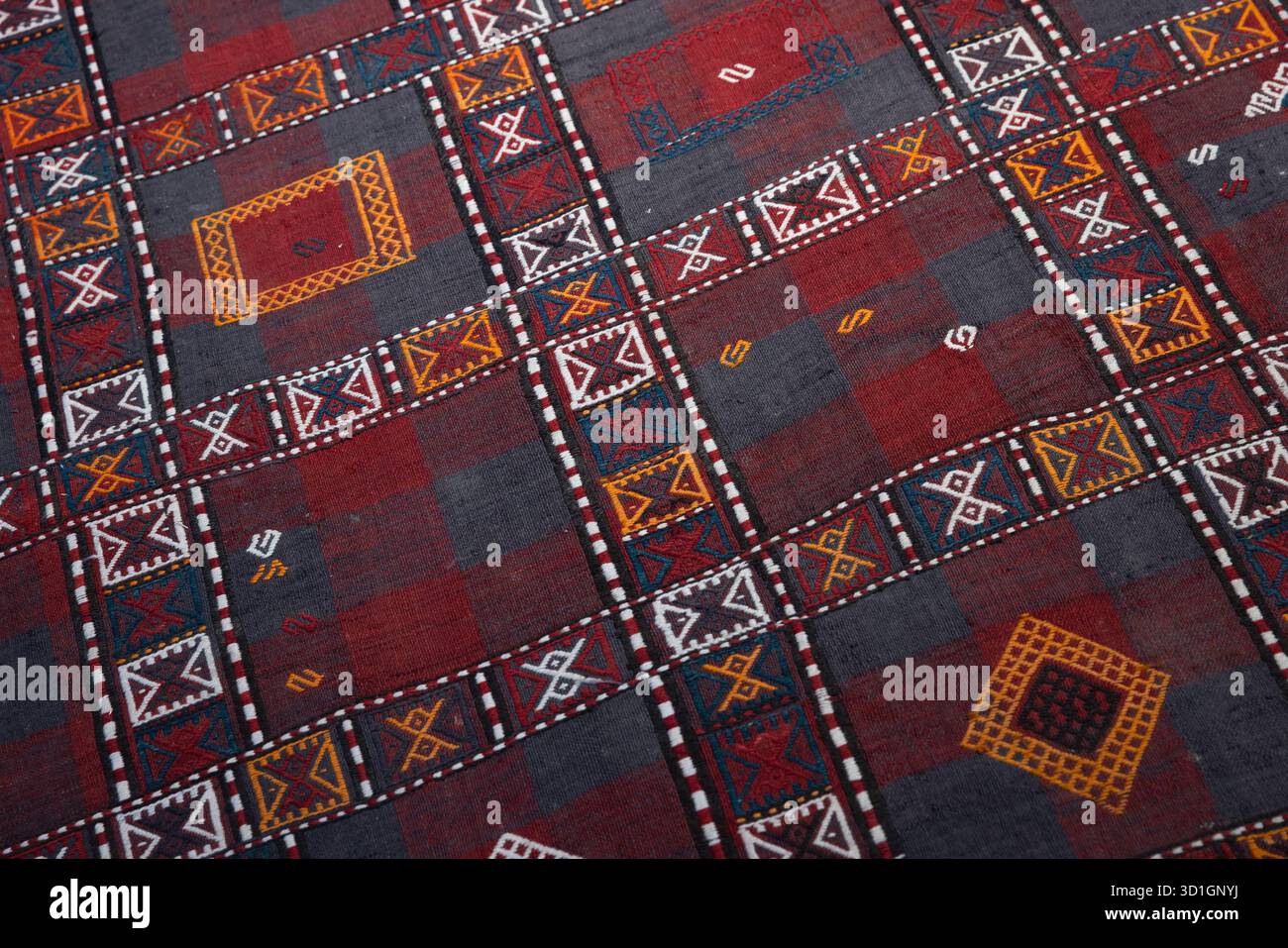 Un tessuto vivace caratterizzato da una griglia geometrica di blocchi rossi e grigi, delimitata da intricati motivi bianchi e colorati. Antico tappeto orientale Foto Stock