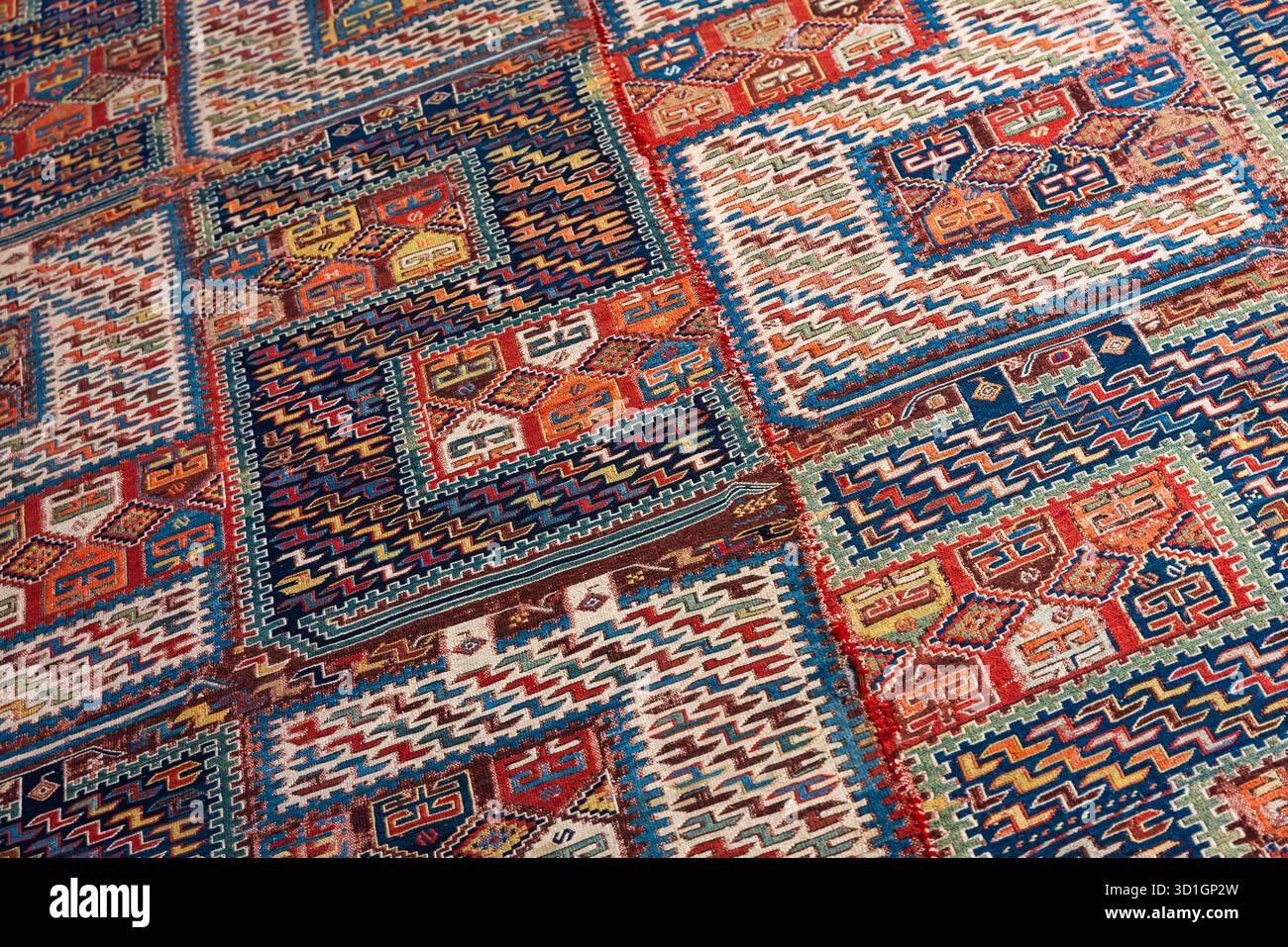 Un antico tappeto in tessuto a mano riccamente decorato, caratterizzato da audaci blocchi di colore, bordi a zigzag e intricati motivi geometrici. Ideale per aggiungere calore e consistenza Foto Stock