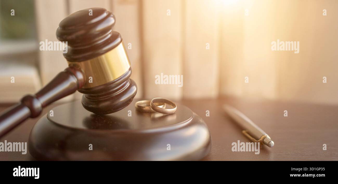 Un giudice di legno gavel su un tavolo accanto a due fedi nuziali e una penna, simboleggiando le questioni legali relative al matrimonio o al divorzio Foto Stock